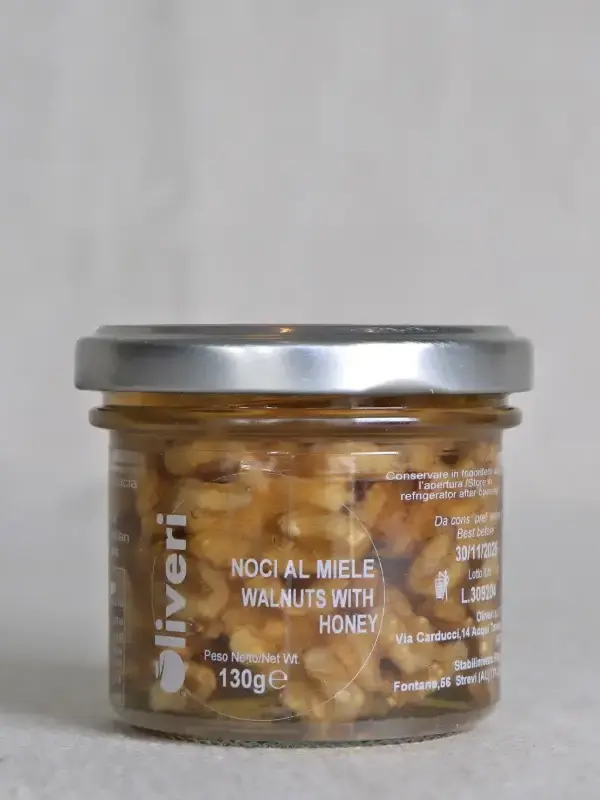 Glass med italienske valnøtter i akasiehonning fra Oliveri, plassert på et trebord med ost og nøtter.