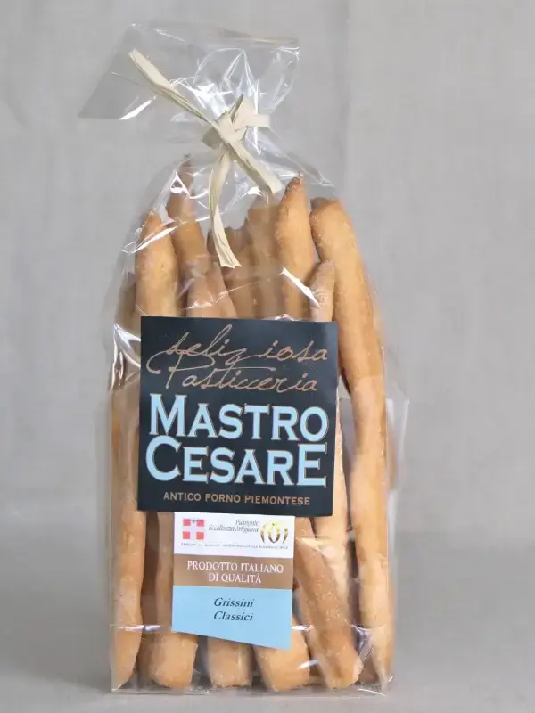 Pakke med håndlagde Grissini Classici fra MastroCesare, servert med ost, skinke og oliven på et trebord.
