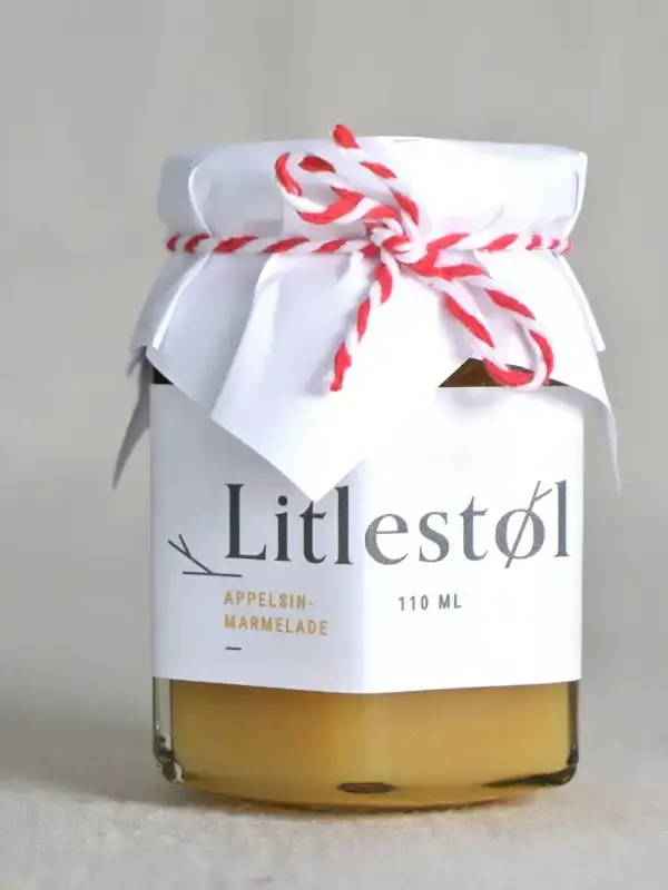 Glass med Litlestøl appelsinmarmelade 110ml, plassert på et trebord med ferskt brød og smør.