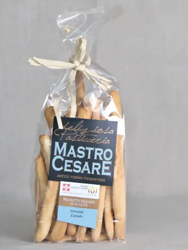 Pakke med håndlagde Grissini al Tartufo fra MastroCesare, servert med ost, spekemat og oliven på et trebord.
