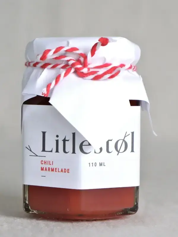 Glass med Litlestøl chilimarmelade 110ml, plassert på et trebord med ost, nøtter og ferskt brød.