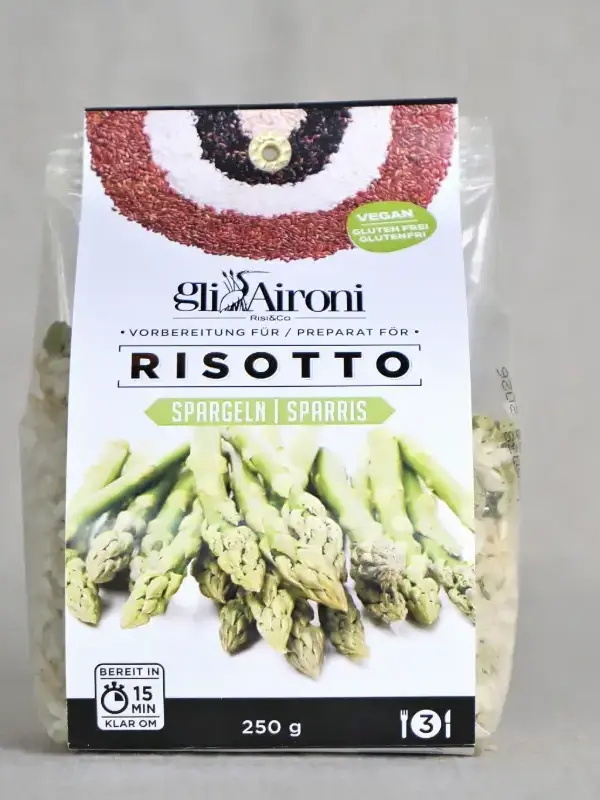 Pakke med Gli Aironi risottomiks med asparges 250g, plassert på kjøkkenbenk med risottoskål, parmesan og hvitvin.