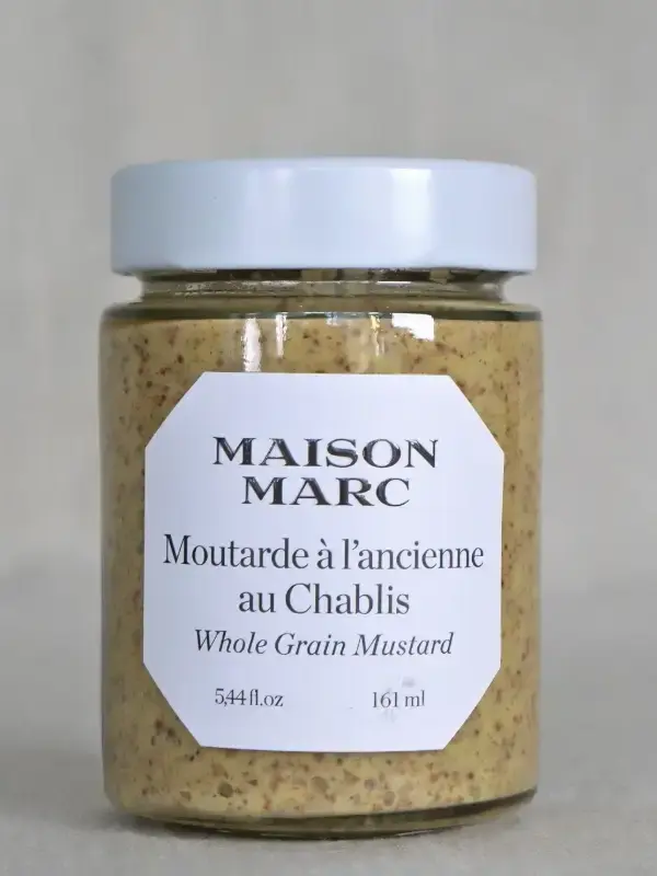 Glass med Maison Marc Chablis grov sennep 170g, plassert på et trebord med baguette og friske urter.