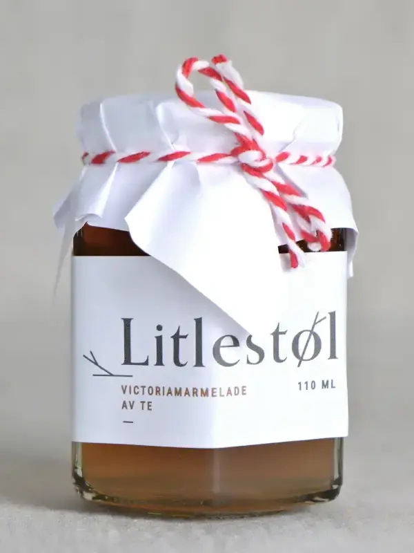 Glass med Litlestøl Victoria Temarmelade 110ml, plassert på et trebord med scones, smør og porselenstallerken.